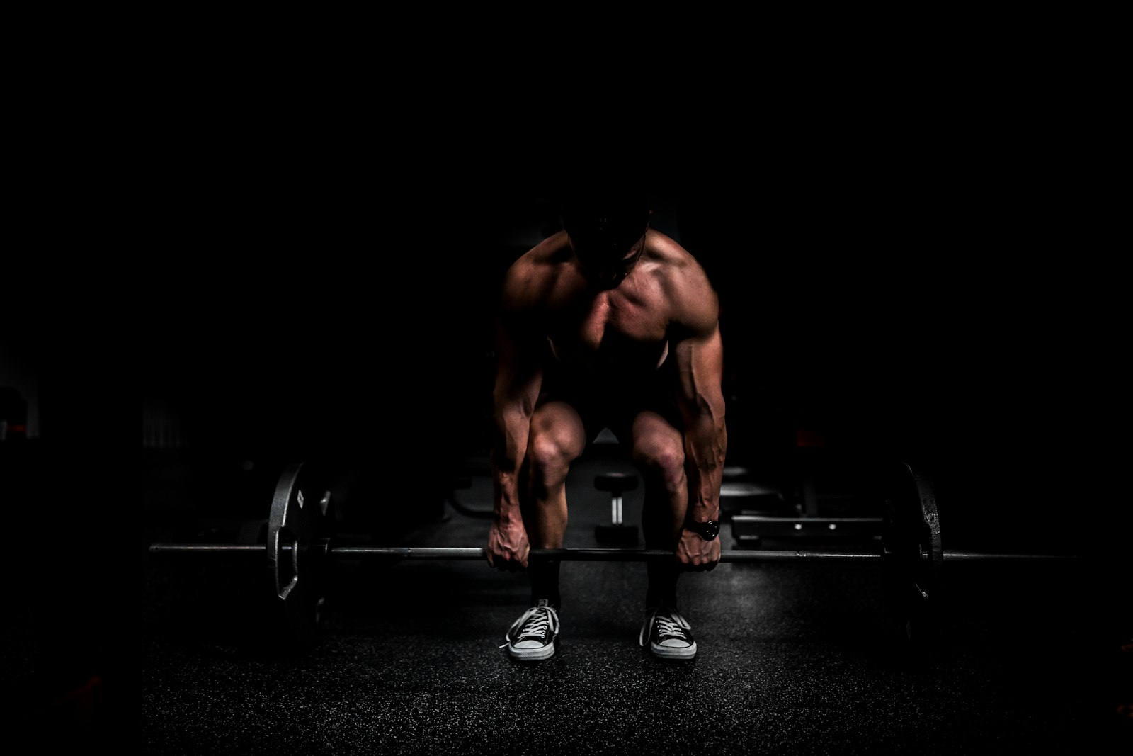 Man hinging over a barbell in a dark gym
